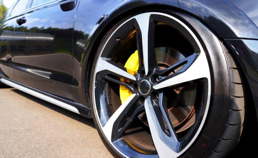 A close-up of the front tire of a blue sports car with low-profile tires and yellow brake calipers on a sunny day.