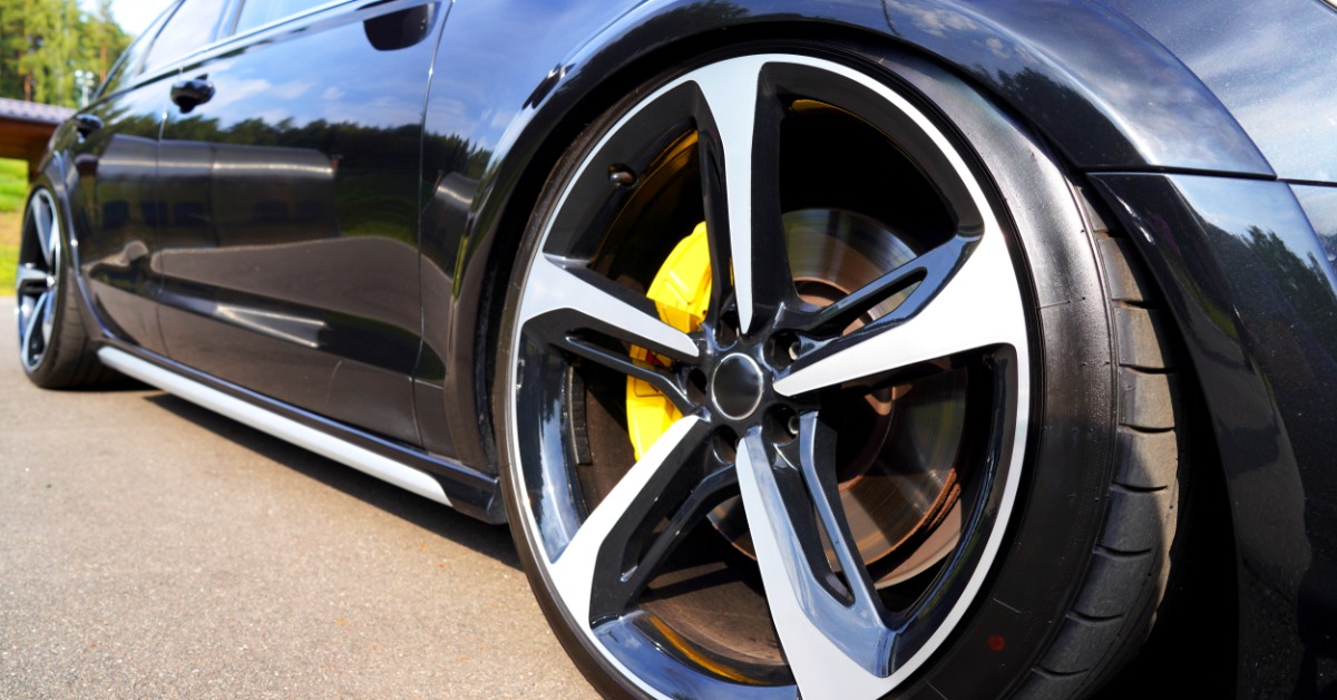 A close-up of the front tire of a blue sports car with low-profile tires and yellow brake calipers on a sunny day.