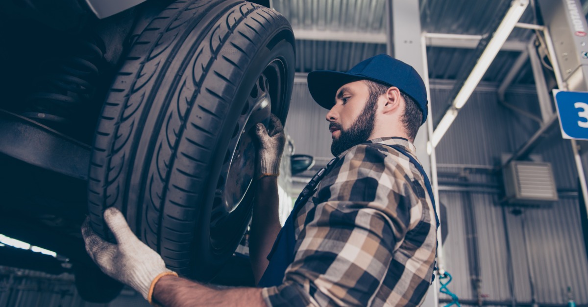 A low-angle view of a man in a flannel shirt with white gloves removing the tire from a car on a lift.