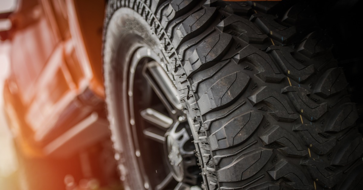A close-up of an off-road tire on the back of a truck. The tire is clean and new with deep treads and grooves.