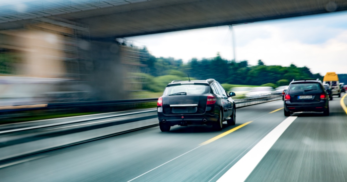 A black car traveling on a multi-lane highway under an overpass with other vehicles and blurred road lines.