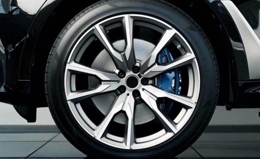 A close-up of a brand-new tire and rim on a shiny, black car. The car is parked on blue tile flooring.