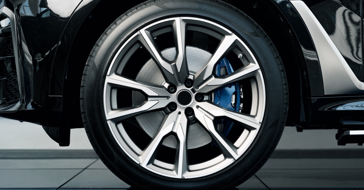 A close-up of a brand-new tire and rim on a shiny, black car. The car is parked on blue tile flooring.
