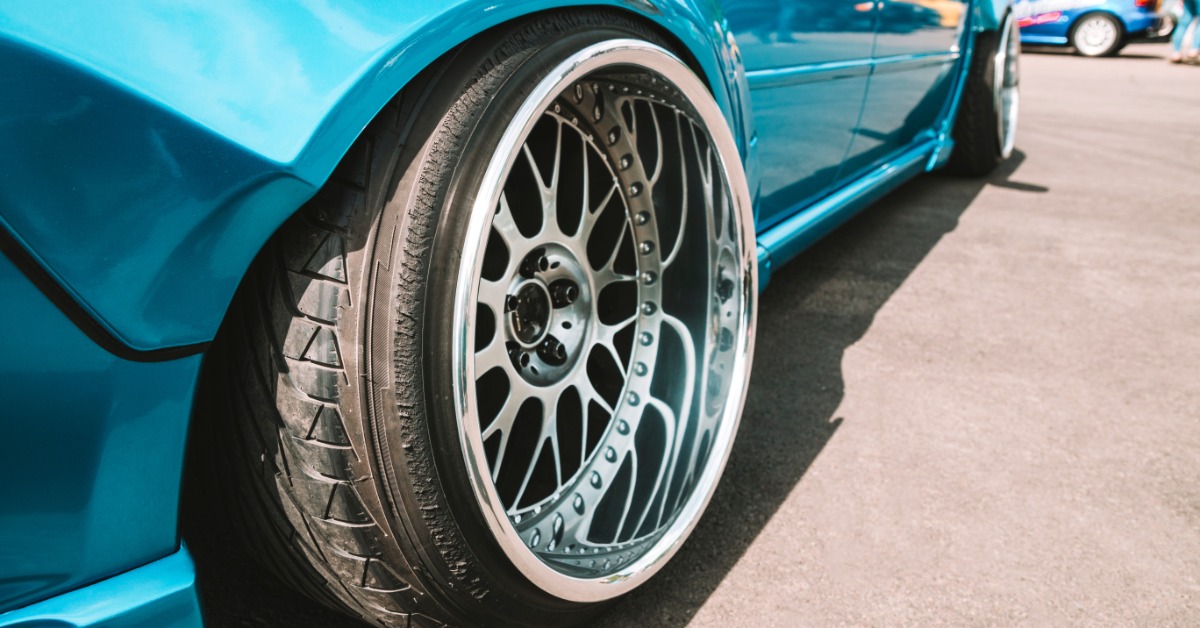 A close-up of a side view of a light blue car. The tires are oversized and custom to give the car a different stance.
