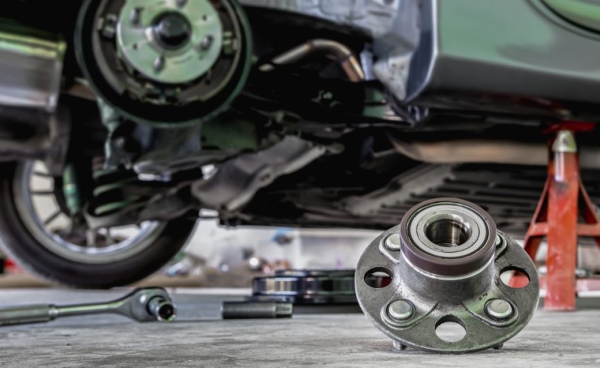 A wheel bearing rests on the floor of an automotive shop. A car is on a jack in the background with a wheel removed.