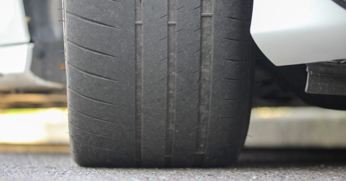 A close-up of a car's tire on pavement with the tread of the vehicle tire worn so much it's almost bald.