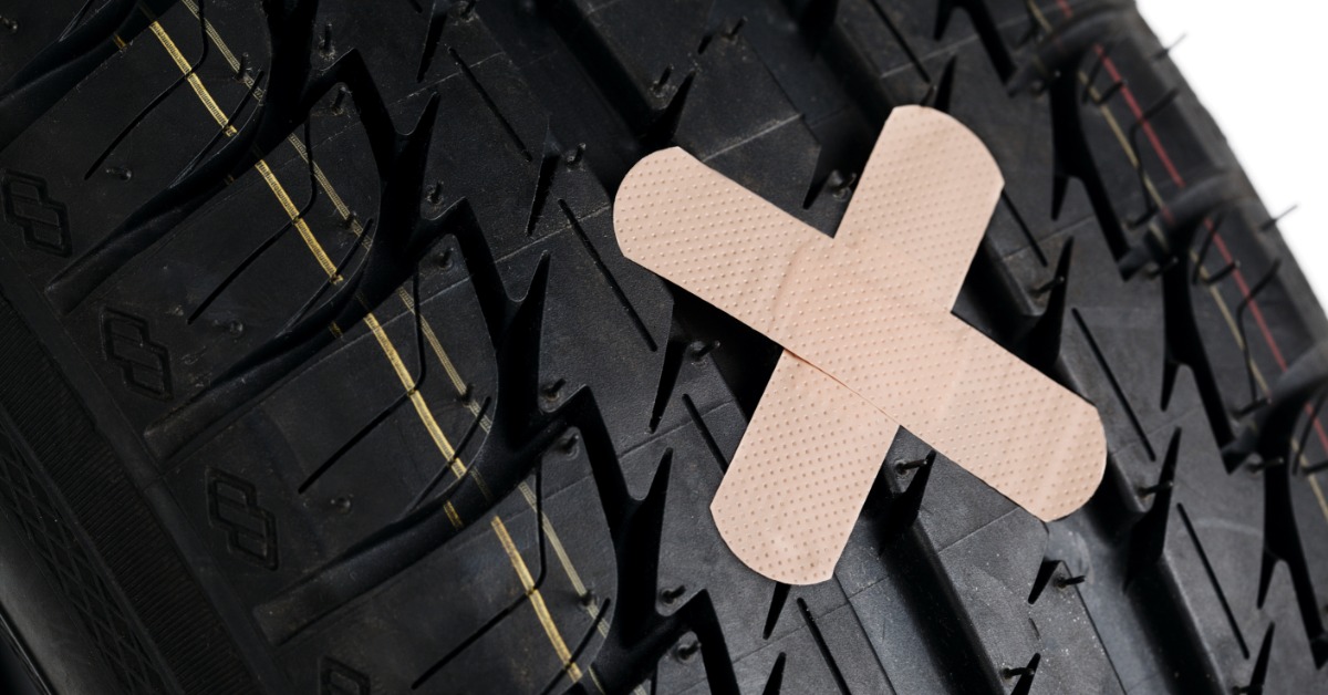 A close-up of a car tire with two band-aids over the tread in a cross pattern on a white background.