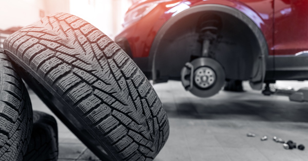 A tire lies sideways against another tire on a shop floor. A red vehicle with the front tire missing is blurred.