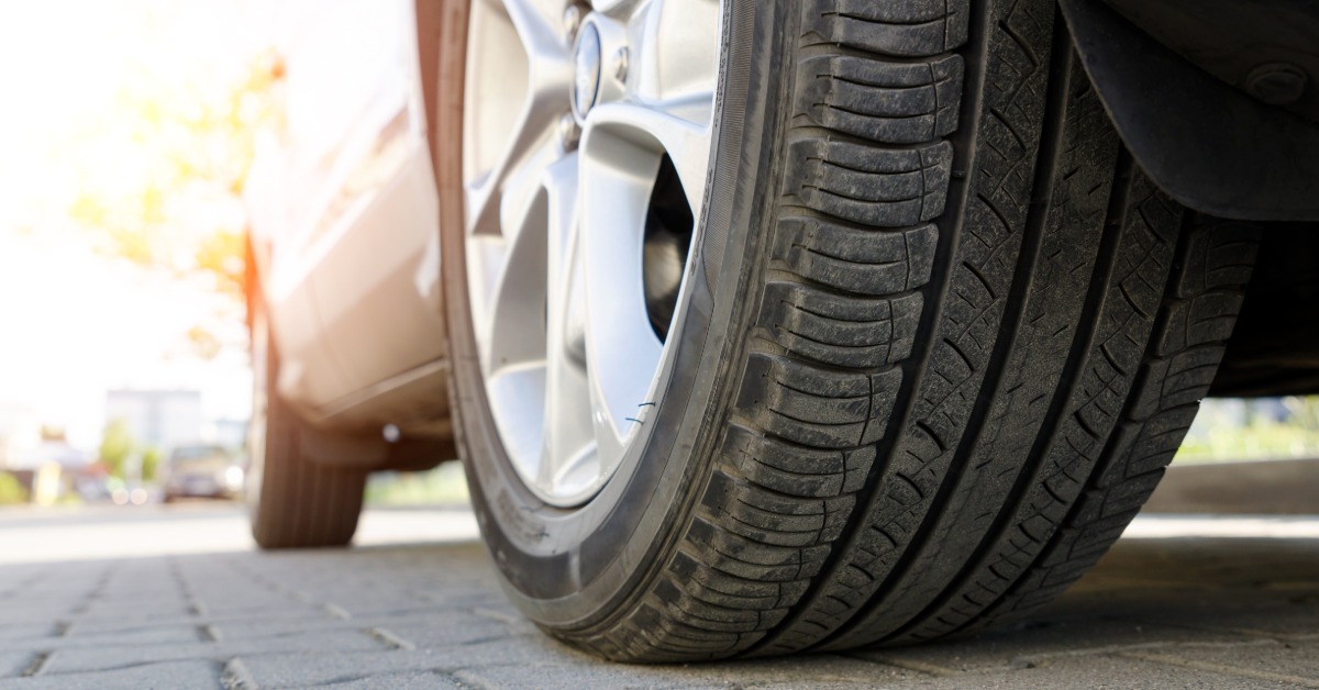A close-up of the side of a vehicle and its rear tire parked in a driveway. The rubber on the tire looks dirty.