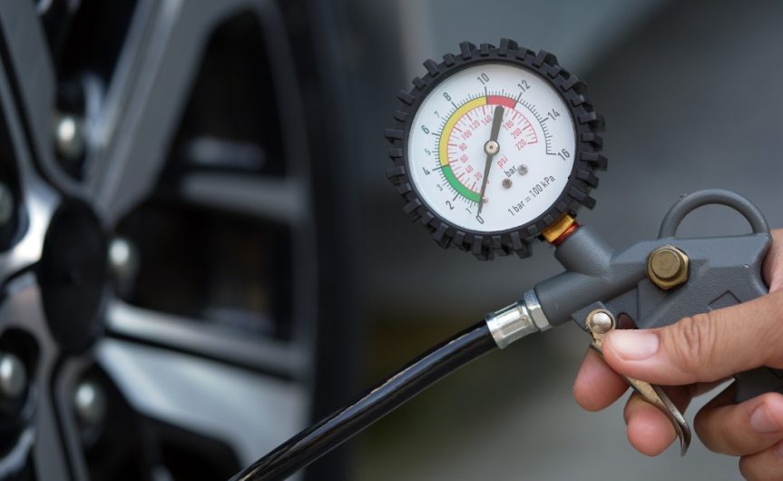 A close-up of the tire pressure gauge that a person is holding up to a car tire with the needle at zero.