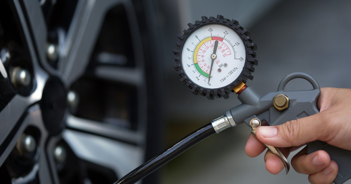 A close-up of the tire pressure gauge that a person is holding up to a car tire with the needle at zero.