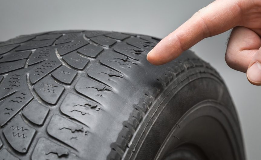 A close-up of someone pointing their finger at the outer edge of a tire. The edge is completely worn and smooth.