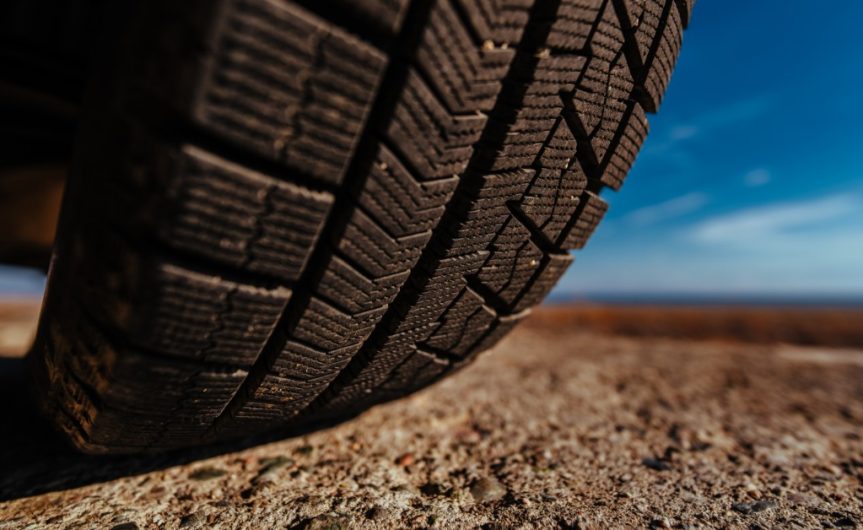 A close-up of the underside of a tire resting on pavement, clearly showing the tread. The sky is blurred in the background.