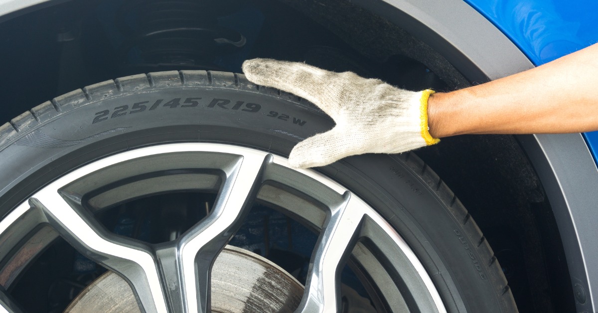 Someone wearing a dirty white glove rests it on a tire secured to a vehicle. The tire sidewall says "225/45 R19 92 W."
