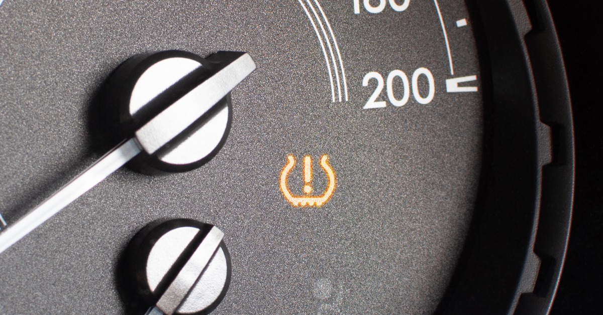 A close-up of the tachometer of a modern car with the tire pressure monitoring system alert light activated.