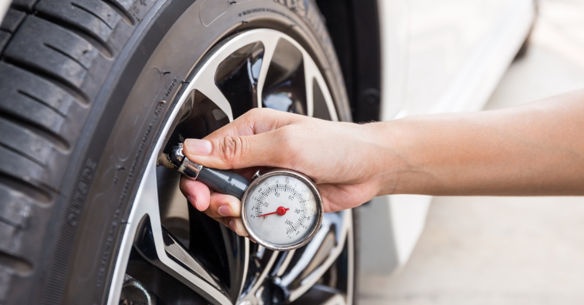 A close-up of a hand holding a tire pressure gauge up to the valve stem of a car tire to check its pressure.