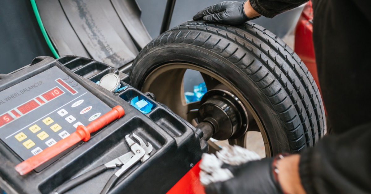 A close-up of a man with black gloves placing a car tire and wheel on a digital wheel balancer in a car workshop.