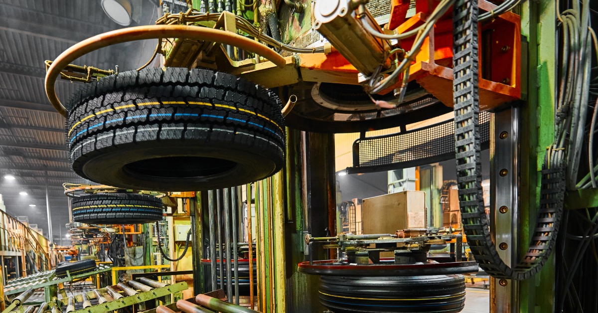 A close-up of a machine at a tire manufacturing facility holding up a brand-new tire above a roller conveyor line.