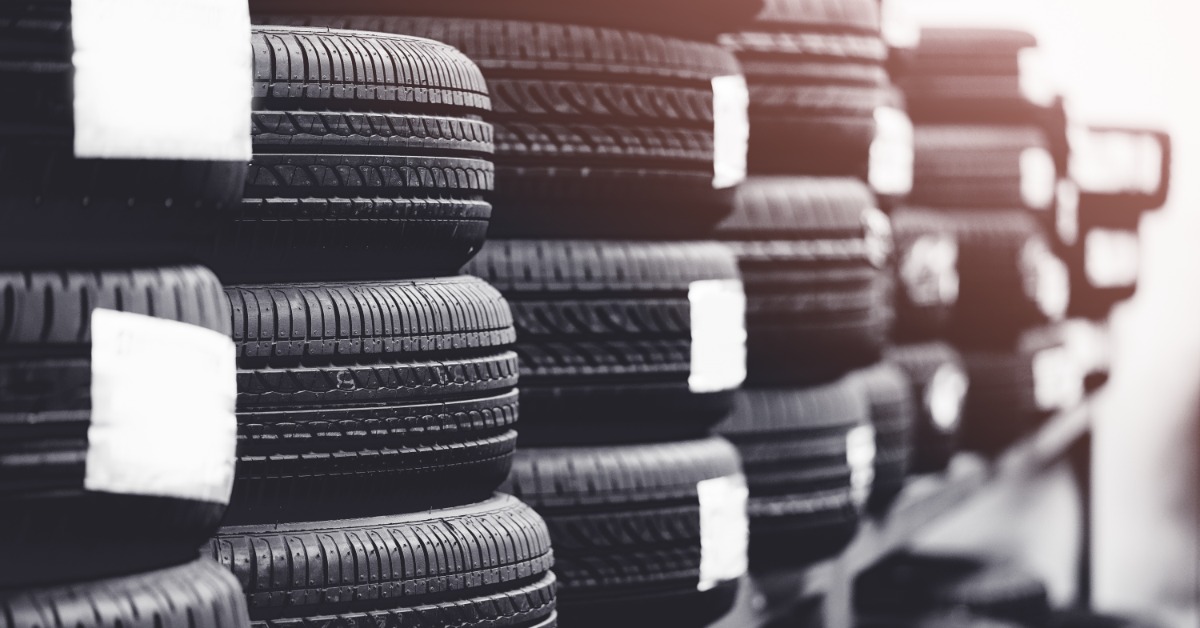 A close-up of numerous brand-new automotive tires stacked neatly into columns with stickers on steel racks.