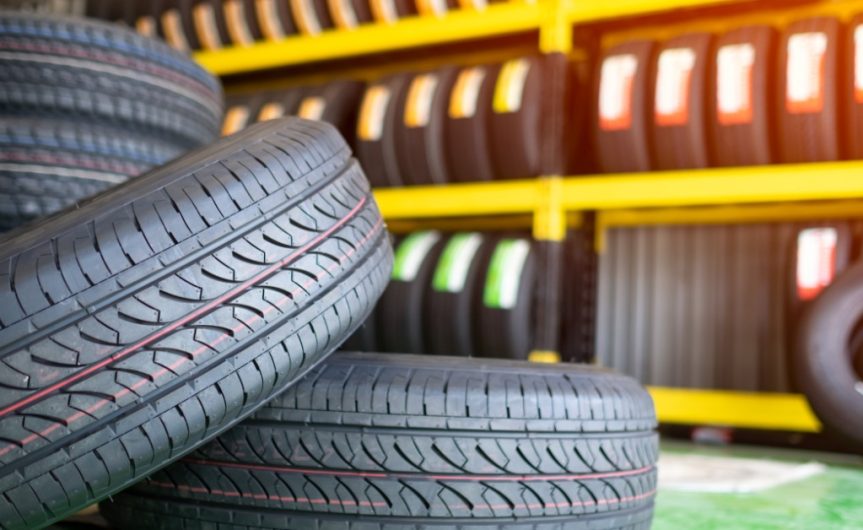 Two small car tires on a green floor next to another pile of tires beside a large yellow shelving unit.