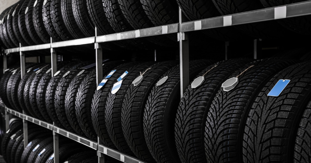 A long metal shelving rack in a tire shop. The rack has three shelves full of black tires with different treads.
