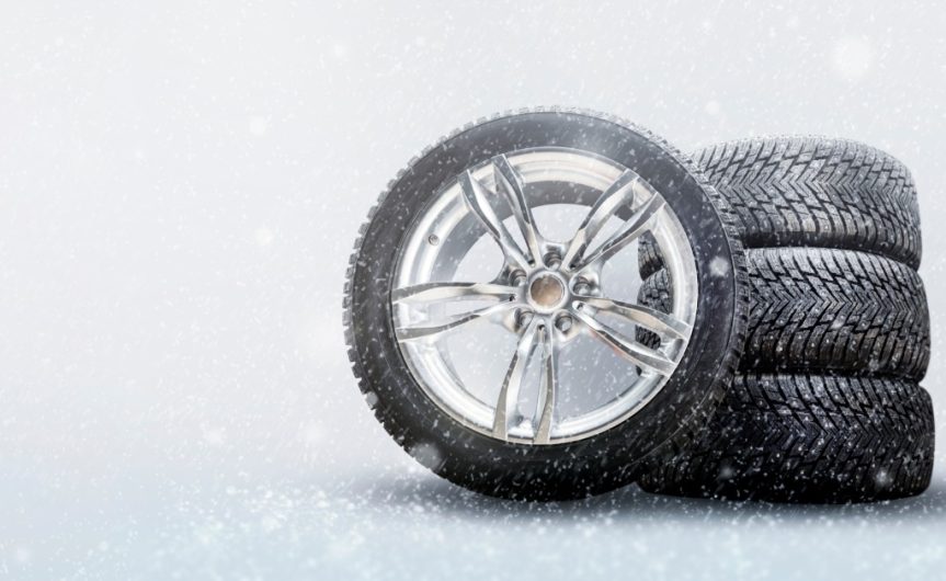 A set of four automotive winter tires against a blank grey background with snow falling in front of them.