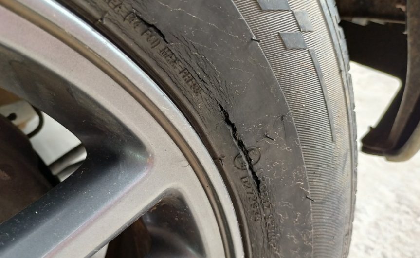 A cracked tire attached to a car outside on a snowy day. The tire has a long crack along its sidewall.