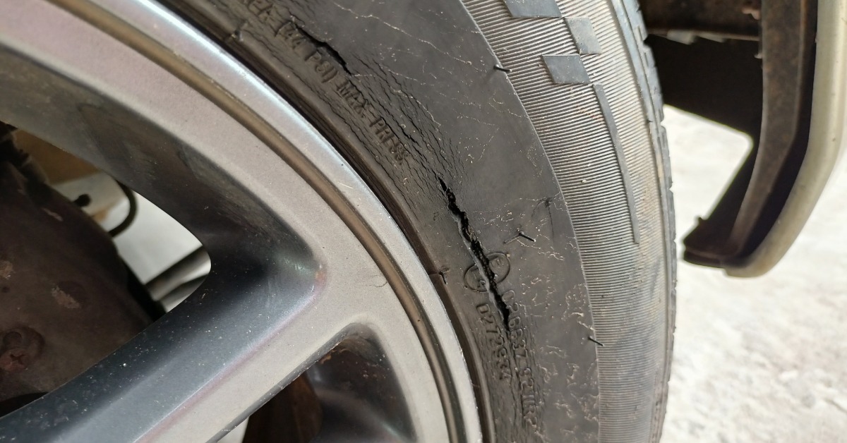 A cracked tire attached to a car outside on a snowy day. The tire has a long crack along its sidewall.