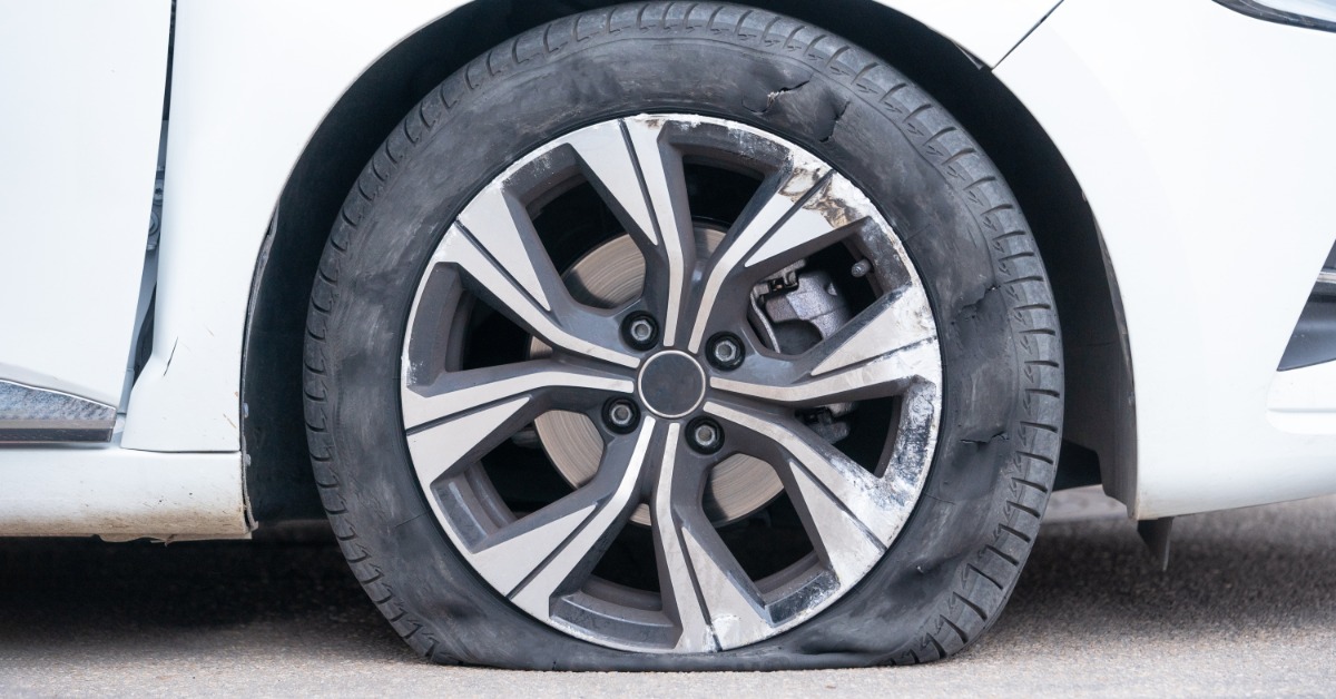A white car parked on the street outside. The front passenger-side tire on the vehicle is completely flat.
