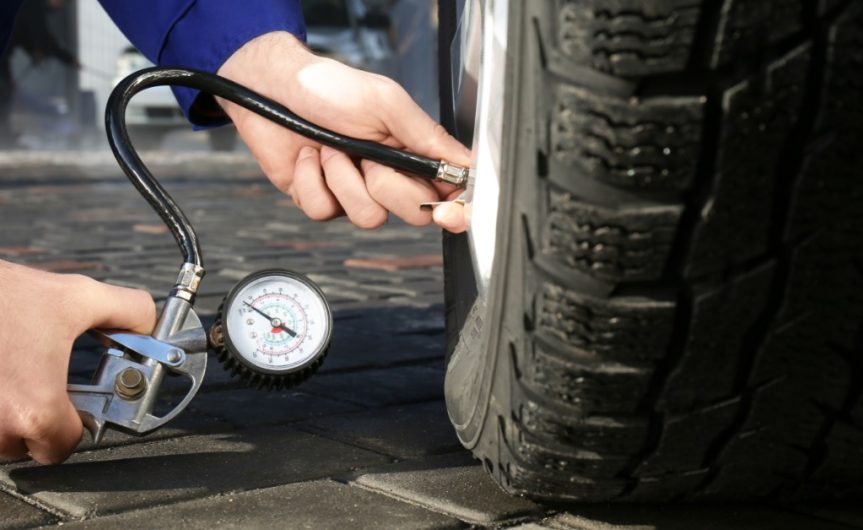 A close-up, ground-level view of a person using a tire air pressure gauge to check the pressure of a car tire.