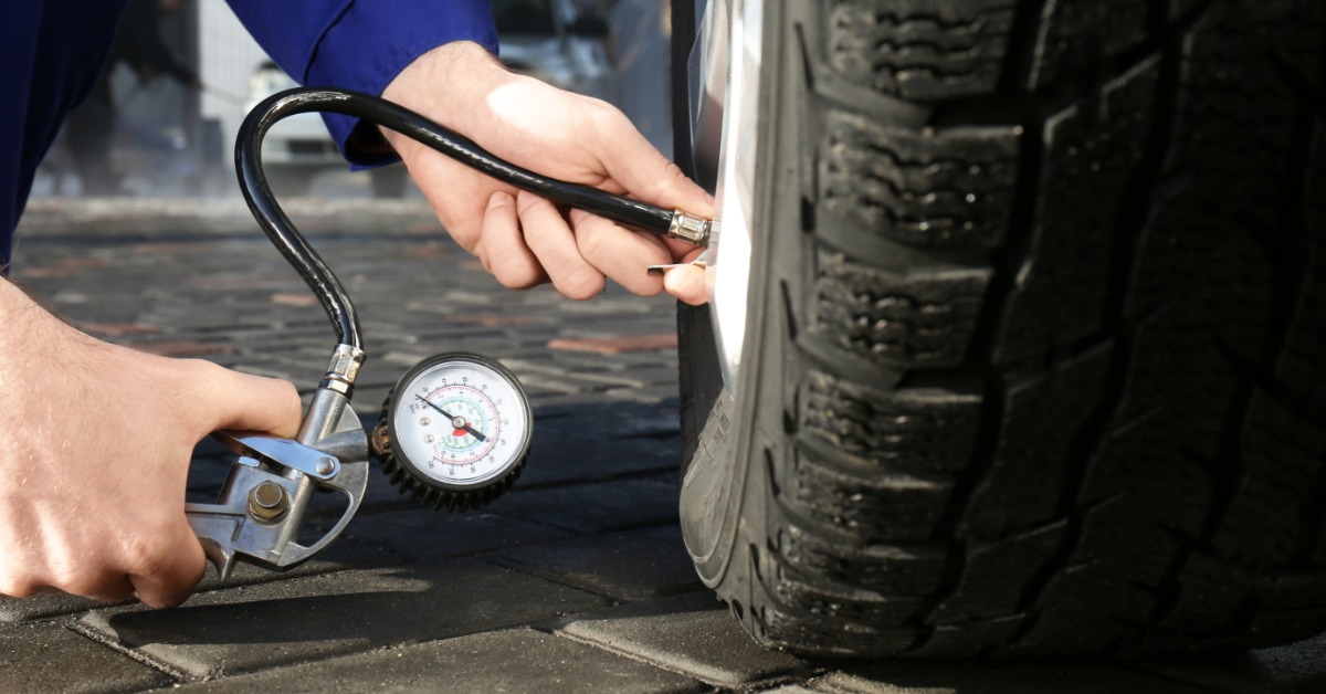A close-up, ground-level view of a person using a tire air pressure gauge to check the pressure of a car tire.