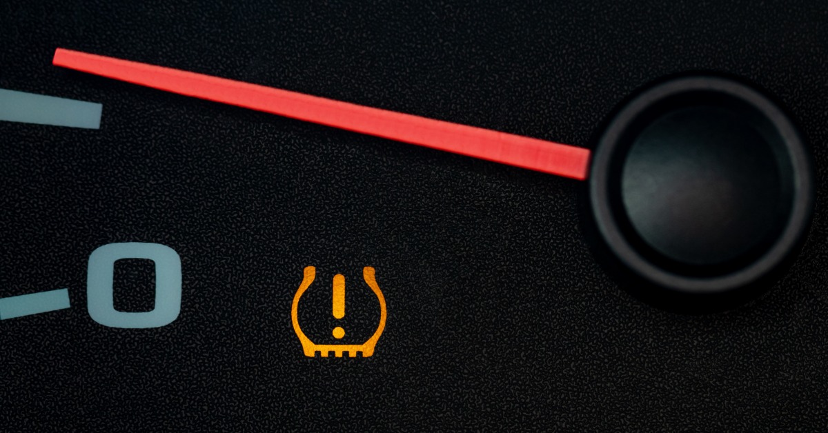 A close-up of the red dial face of a tachometer with the tire pressure monitoring system warning light activated.