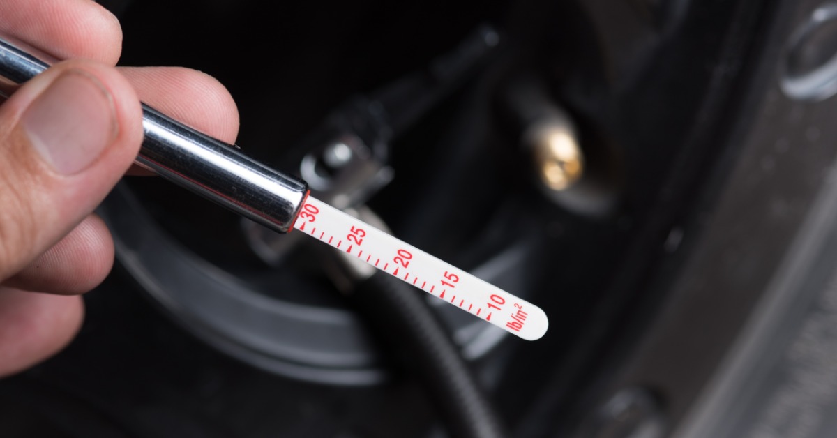 A close-up of a hand holding a manual tire pressure gauge with the meter showing the tire is at 30 PSI.