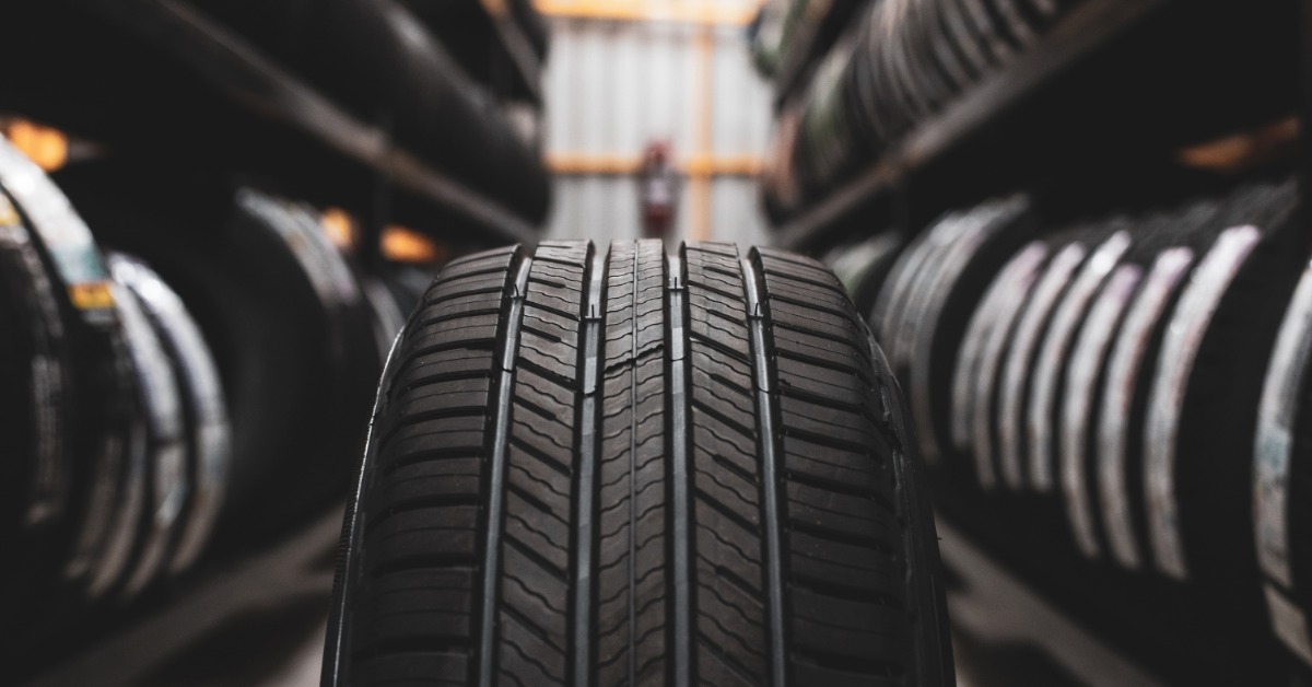 A clean new tire standing in a brightly lit aisle of a shop with tall shelves full of new vehicle tires.