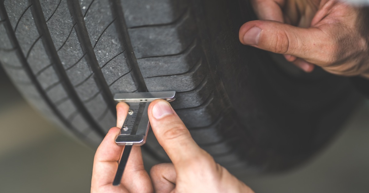 A close-up of a person's hands as they hold up a tire tread depth tool to check the tread of a car's tires.