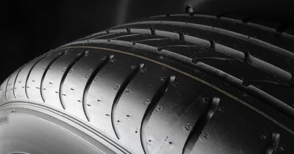 A close-up of the top half tread of a new summer car tire with sipes and grooves against a black background.