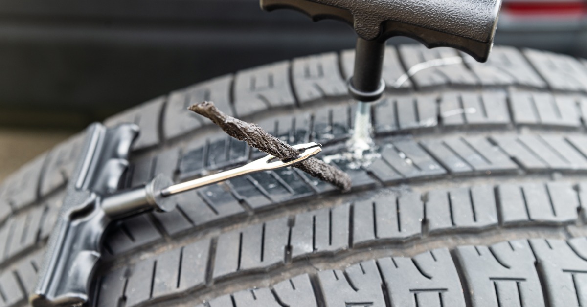 A close-up of tire plug repair kit tools on the surface of a car tire, with the spiral reamer embedded in the tread.