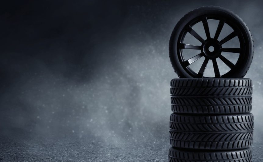 A black tire standing upright on a stack of three more black tires. White fog fills the area behind the stack.