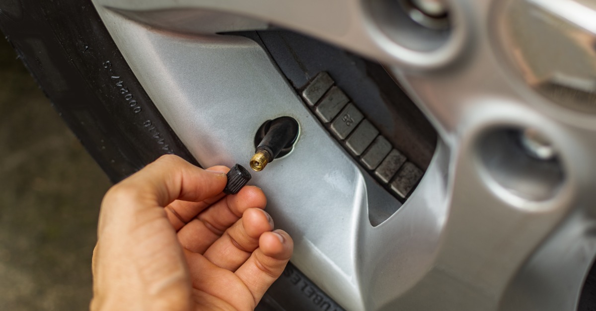 A close-up of a hand removing the cap from the tire valve of an automotive tire and showing the brass nozzle.