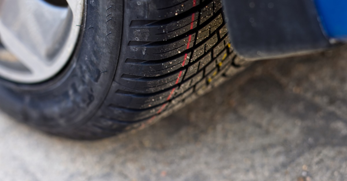 A car parked outside during the daytime. The driver’s side front tire has a red stripe and yellow stripe on it.