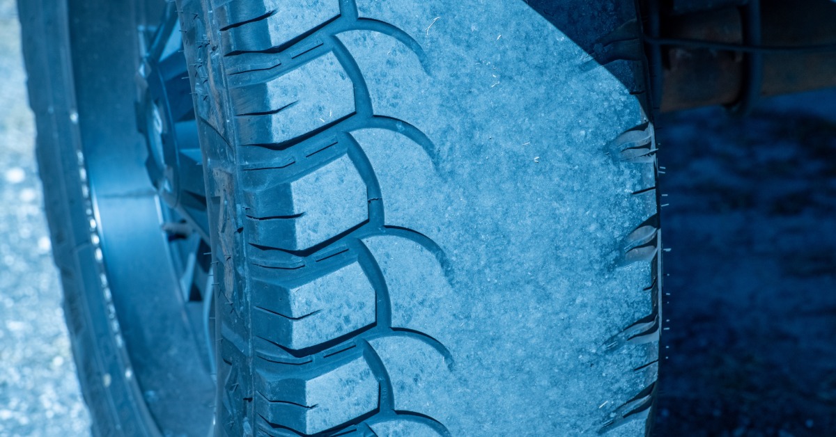 A bright light shining on a black car tire. The tire has a long, thick, flat patch running along the center.