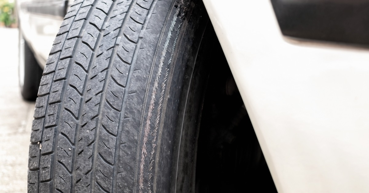 A close-up on the front tire of a white car showing uneven tire wear damage with exposed metal wire cords.