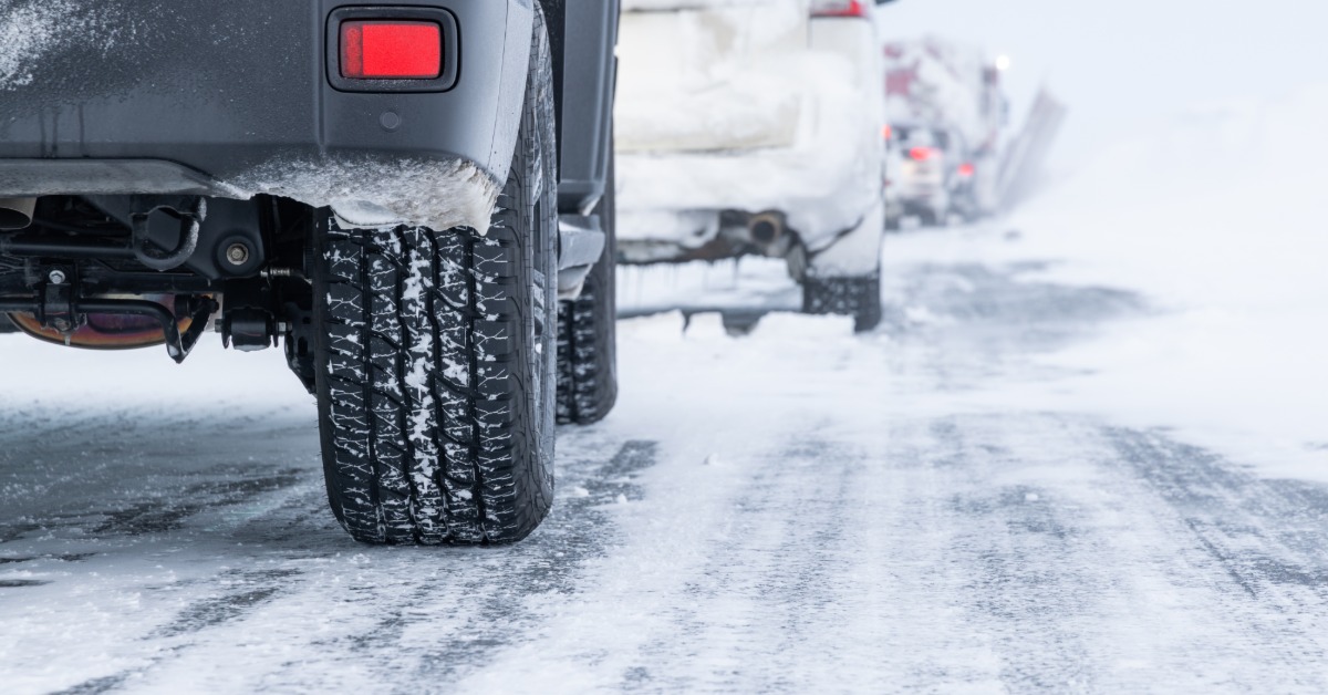 Cars driving on a snow-covered road with slushy tire tracks, snowy wheels, and blurred winter surroundings.