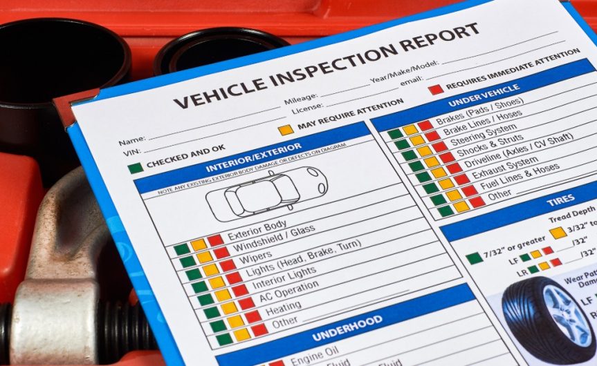 A close-up of a clipboard with a blank vehicle inspection report on it resting on a box of automotive tools.