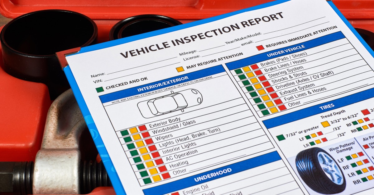 A close-up of a clipboard with a blank vehicle inspection report on it resting on a box of automotive tools.