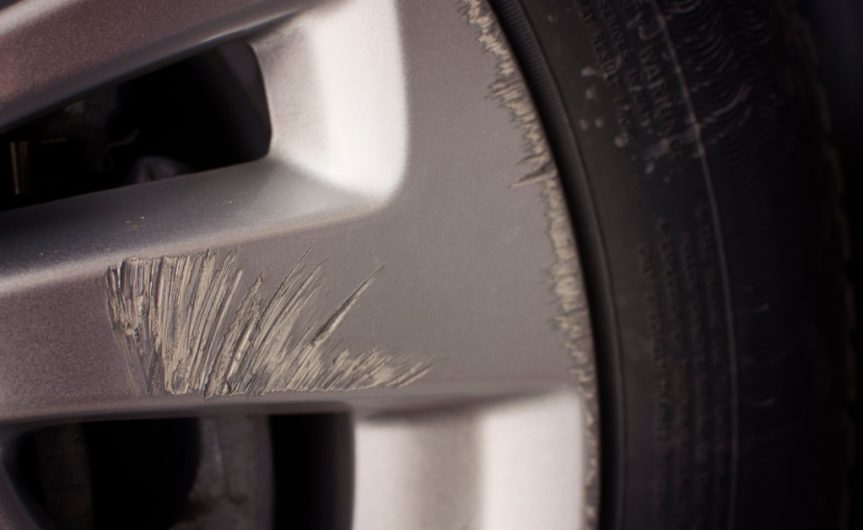 A car wheel with a black tire attached. The wheel has scrapes in its center and along the edges near the rubber.
