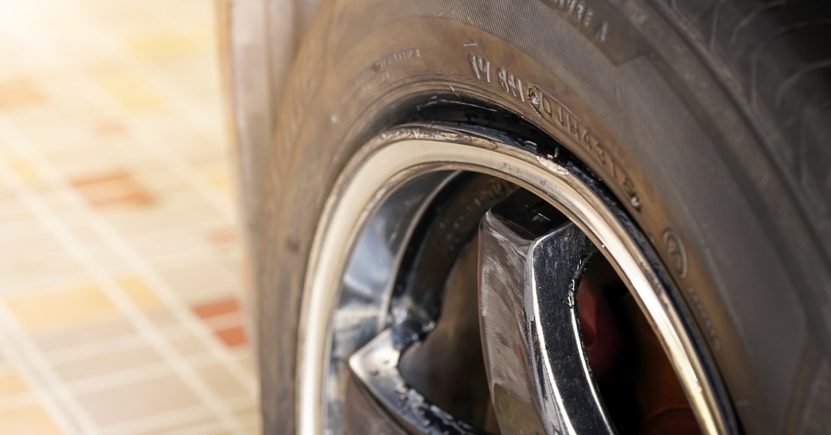 A car parked on a tan tile floor in a brightly lit room. The car has a silver bent rim that is covered in scrapes.