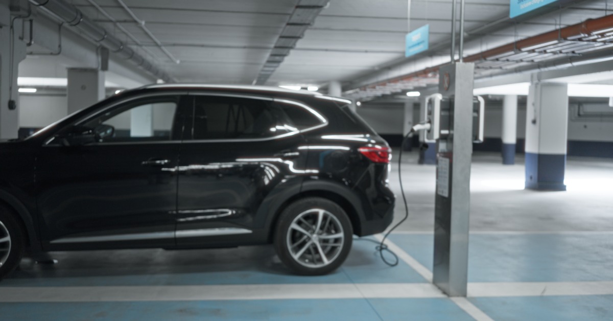 A blurred underground parking garage with electric vehicle charging bays, concrete pillars, and lights.