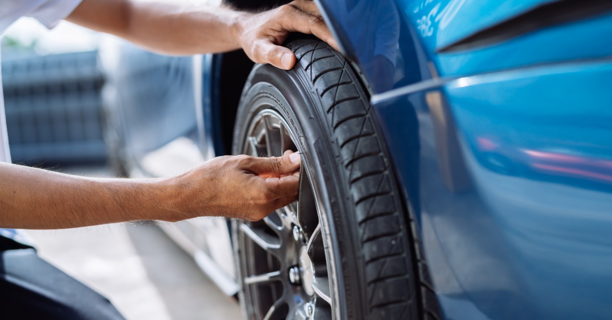 A close-up of the hands of a man crouching down to touch and inspect the wheels and tires of a blue car.