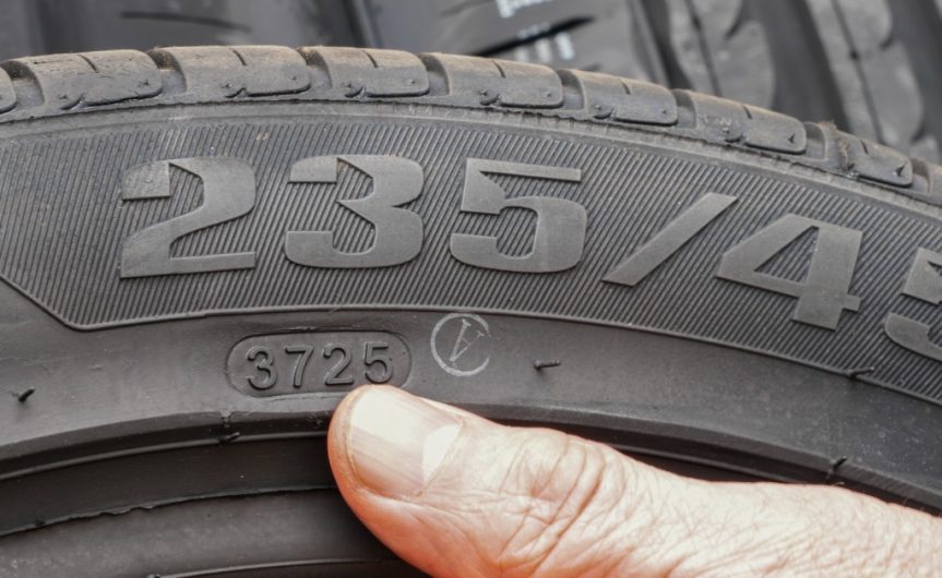 A close-up of a person's thumb pointing to the numbers on a tire's Department of Transportation code.